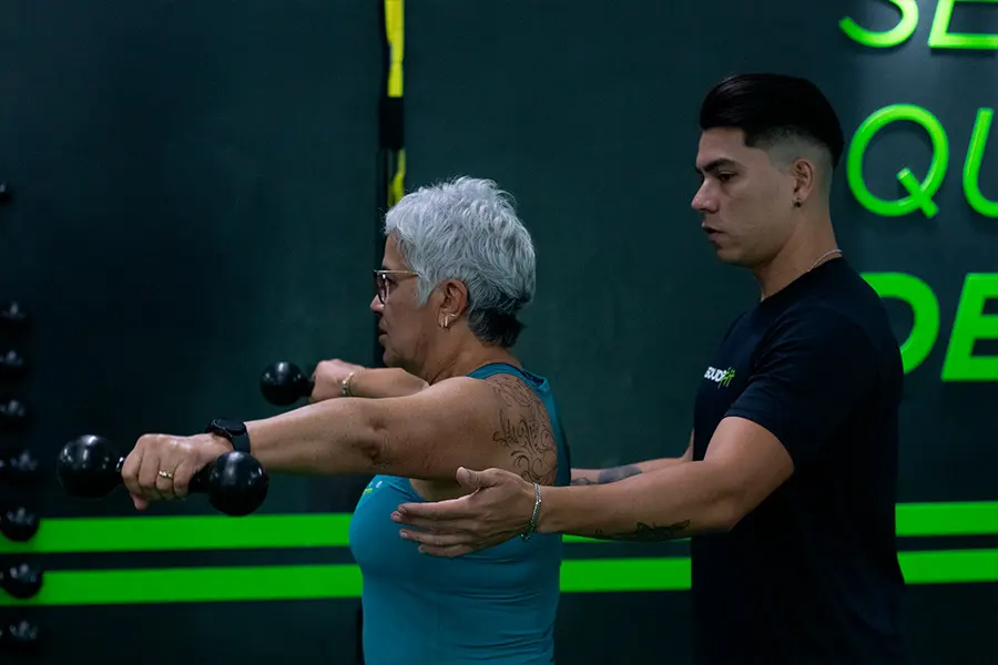 Instrutor da DoctorFit corrigindo a postura de uma aluna durante exercício com halteres